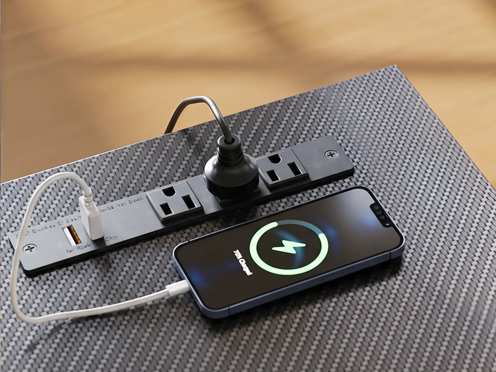 Black desk-mounted power strip with multiple devices plugged in, including USB phone charging, shown on a modern office desk.