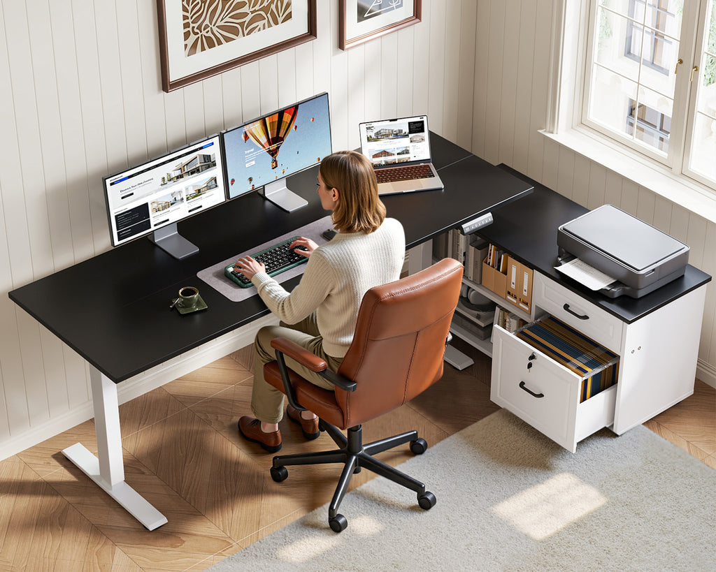 Seated user working at the OffiGo 55-inch black and white standing desk with dual monitors, a laptop and a printer on the file cabinet.
