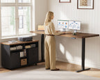 Standing user working at the OffiGo 71-inch executive L-shaped standing desk with a walnut-brown desktop, black legs and a rolling black storage cabinet, with dual monitors and a printer in a sunlit home office.
