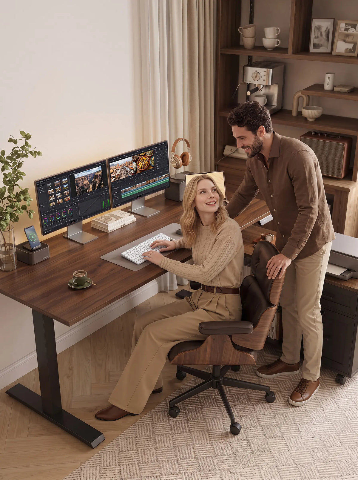 A woman seated at an OffiGo desk with dual monitors showing video editing software, with a man standing beside her.