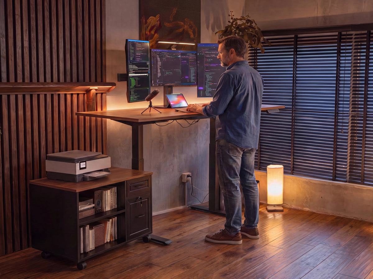 OffiGo standing desk workstation with multiple monitors, file cabinet, and printer shelf in an evening office setup